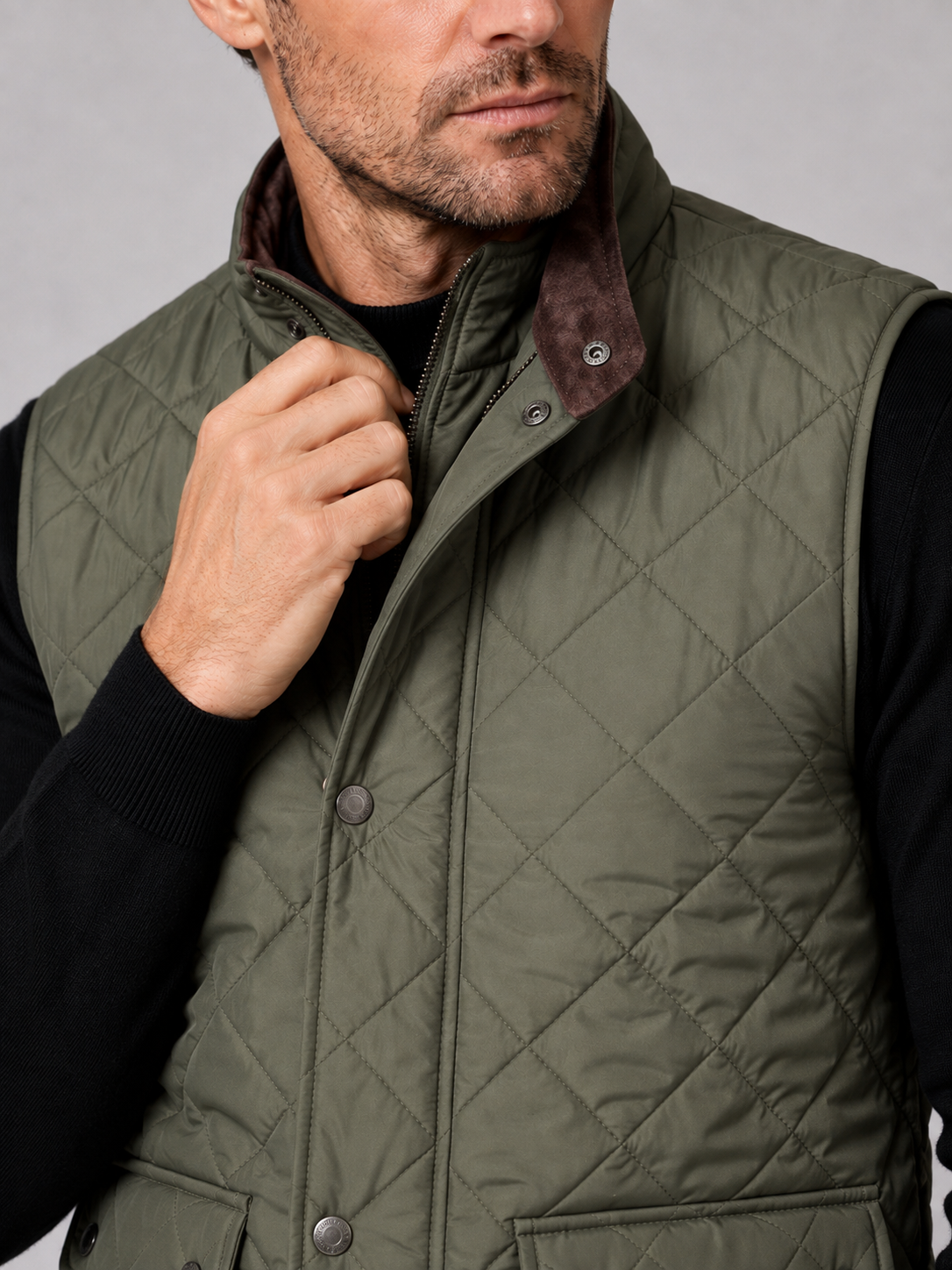 Close-up of an army green quilted vest showing the stitched pattern, polo collar, thick padding, front closure, utility pockets, armholes, and reinforced seams