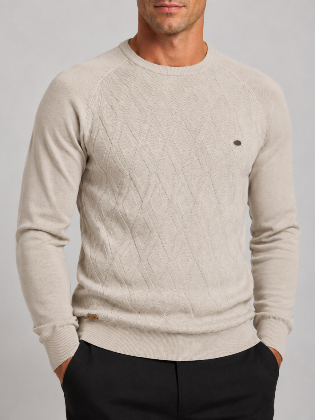 Close-up of a beige argyle sweater showing the diamond knit pattern, crew neckline, ribbed cuffs, hem, and warm texture