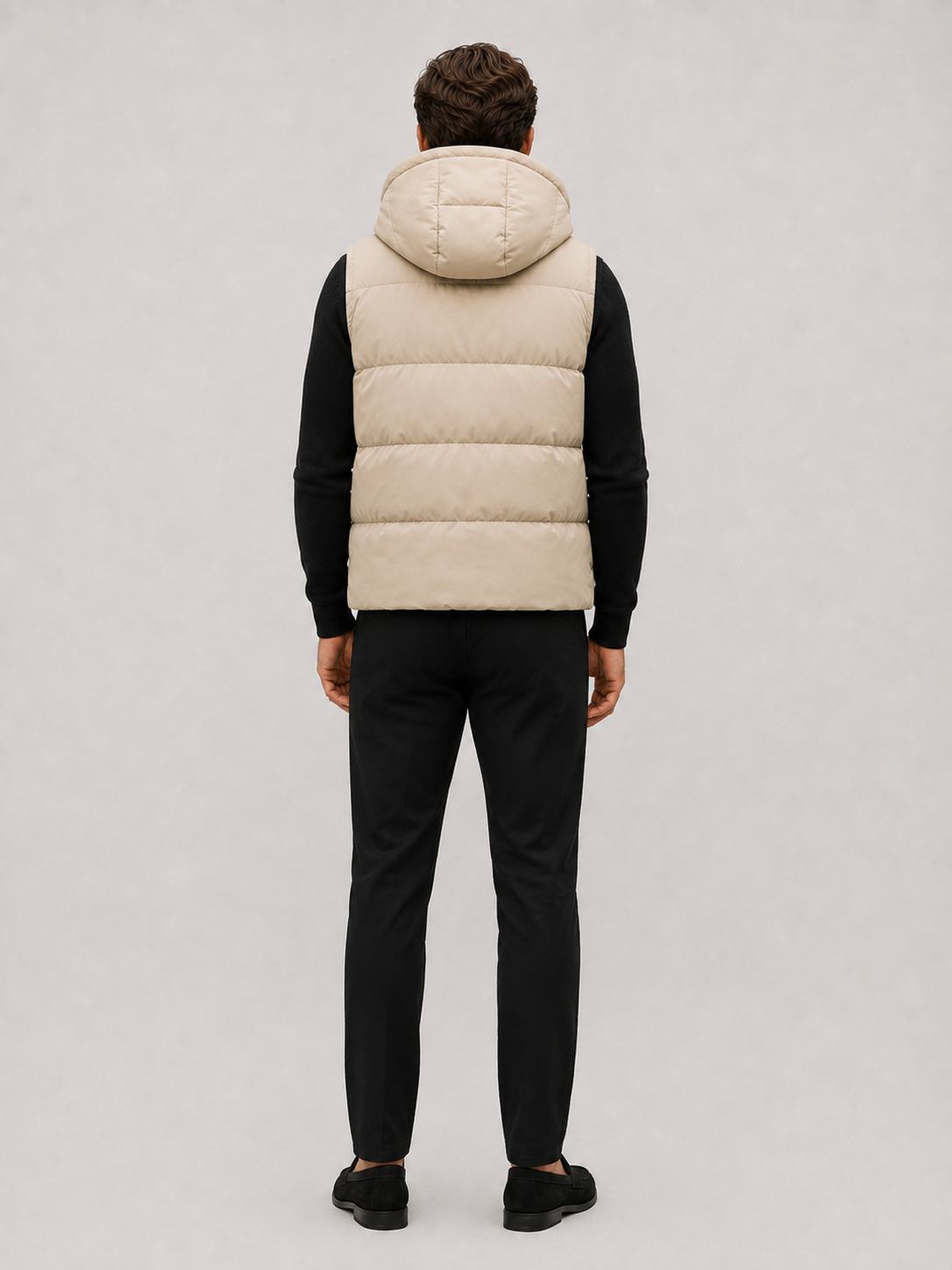 Back view of a man wearing a beige hooded puffer vest showing the attached hood, quilted construction, and comfortable fit