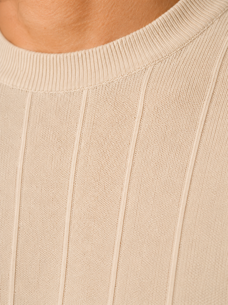 Close up of beige knit t shirt fabric showing soft breathable ribbed texture and refined finish
