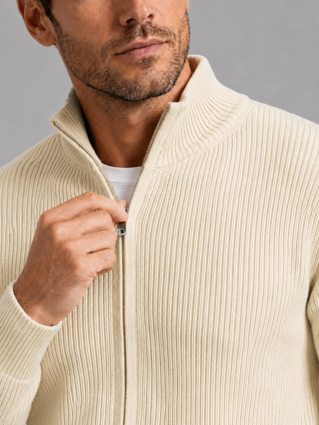Close-up of a beige ribbed knit cardigan showing the textured knit fabric, stand collar, full zipper, ribbed cuffs, hem, and stitching details