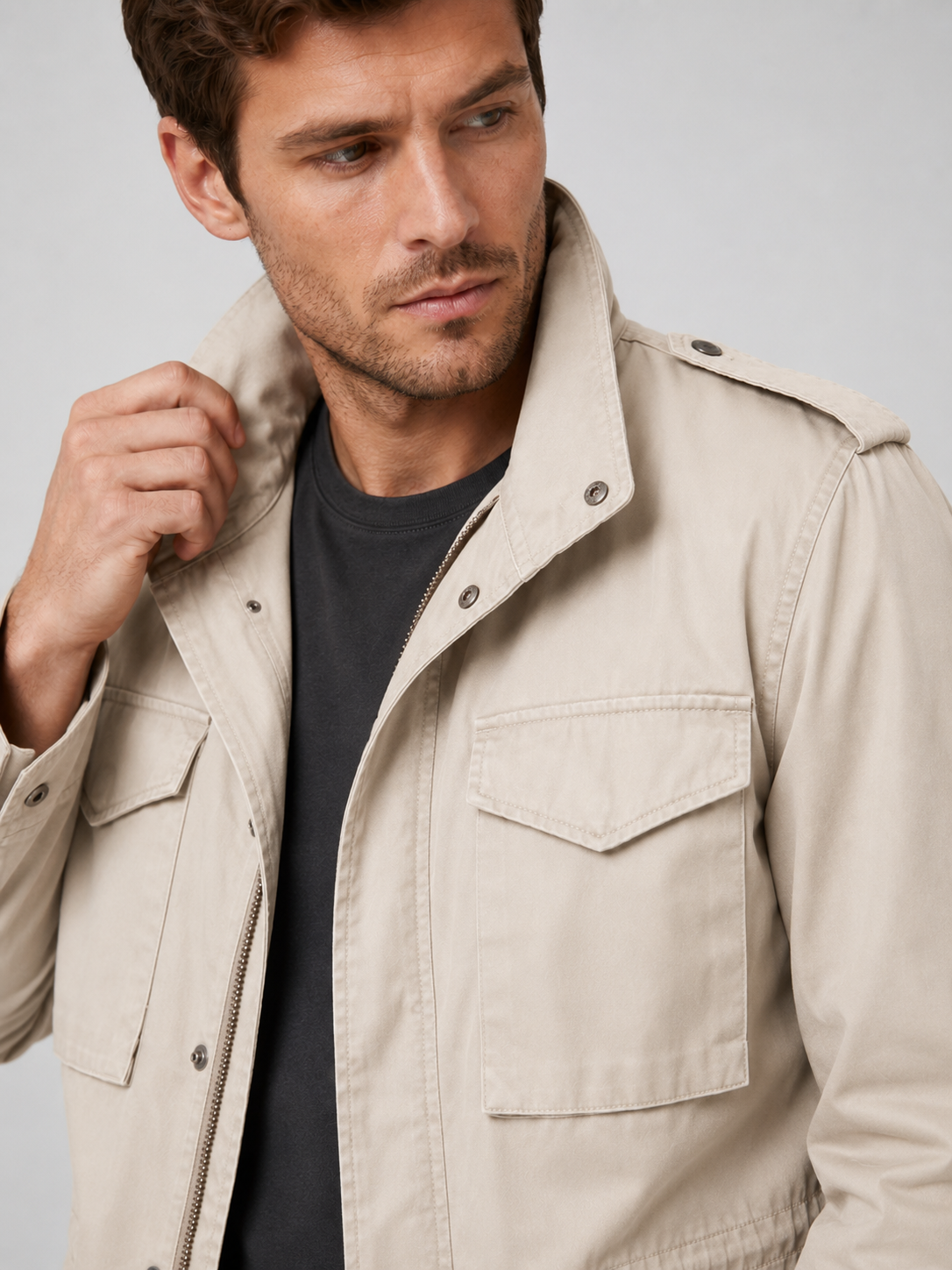 Close up of beige military field jacket showing durable cotton fabric, utility pockets, and zip up front detail