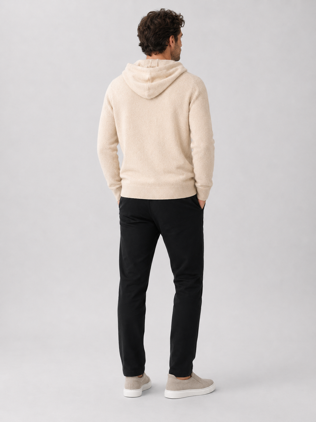 Back view of a man wearing a beige wool hoodie sweater showing the attached hood, long sleeves, and relaxed fit
