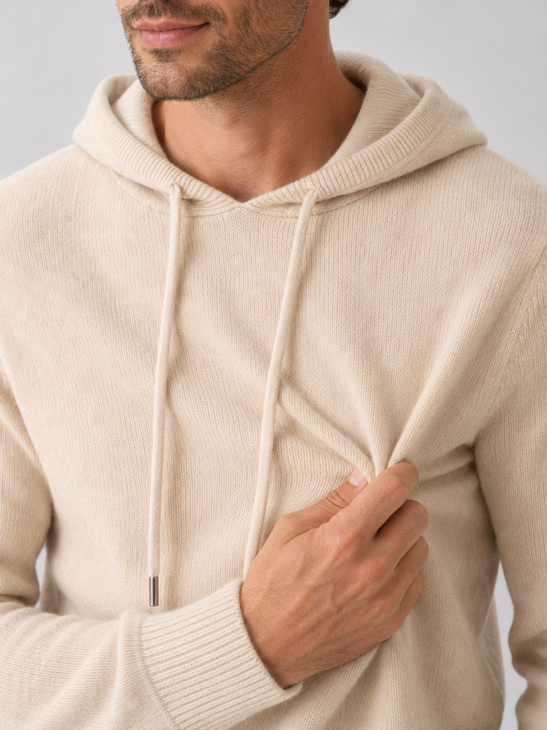 Close-up of a beige wool hoodie sweater showing the soft knit texture, hood, ribbed cuffs, hem, and stitching details