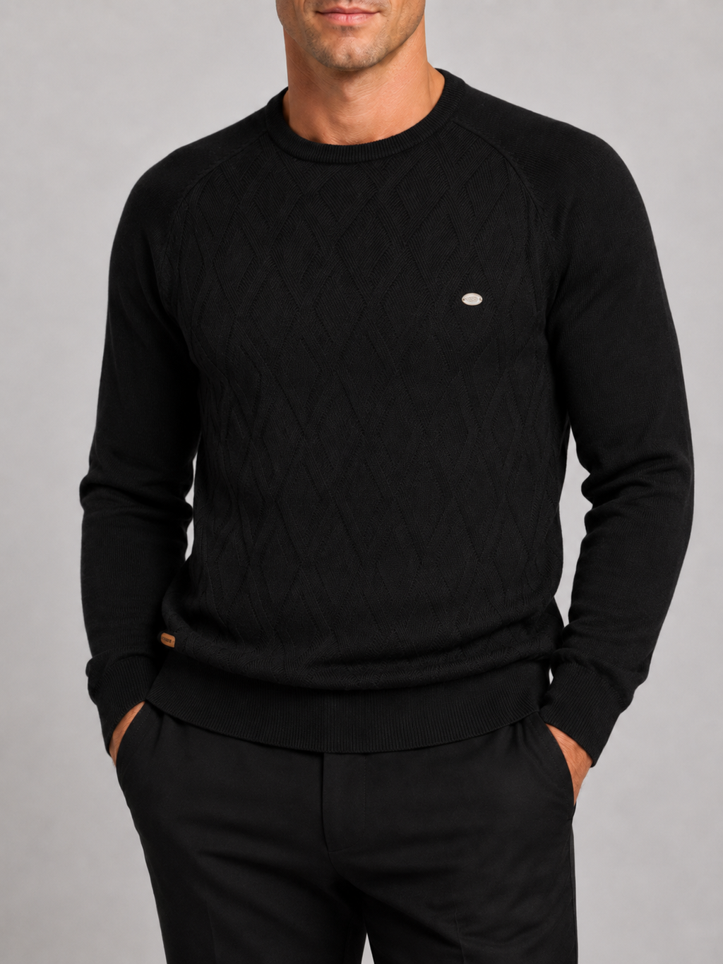 Close-up of a black argyle sweater showing the diamond knit pattern, crew neckline, ribbed cuffs, hem, and warm texture