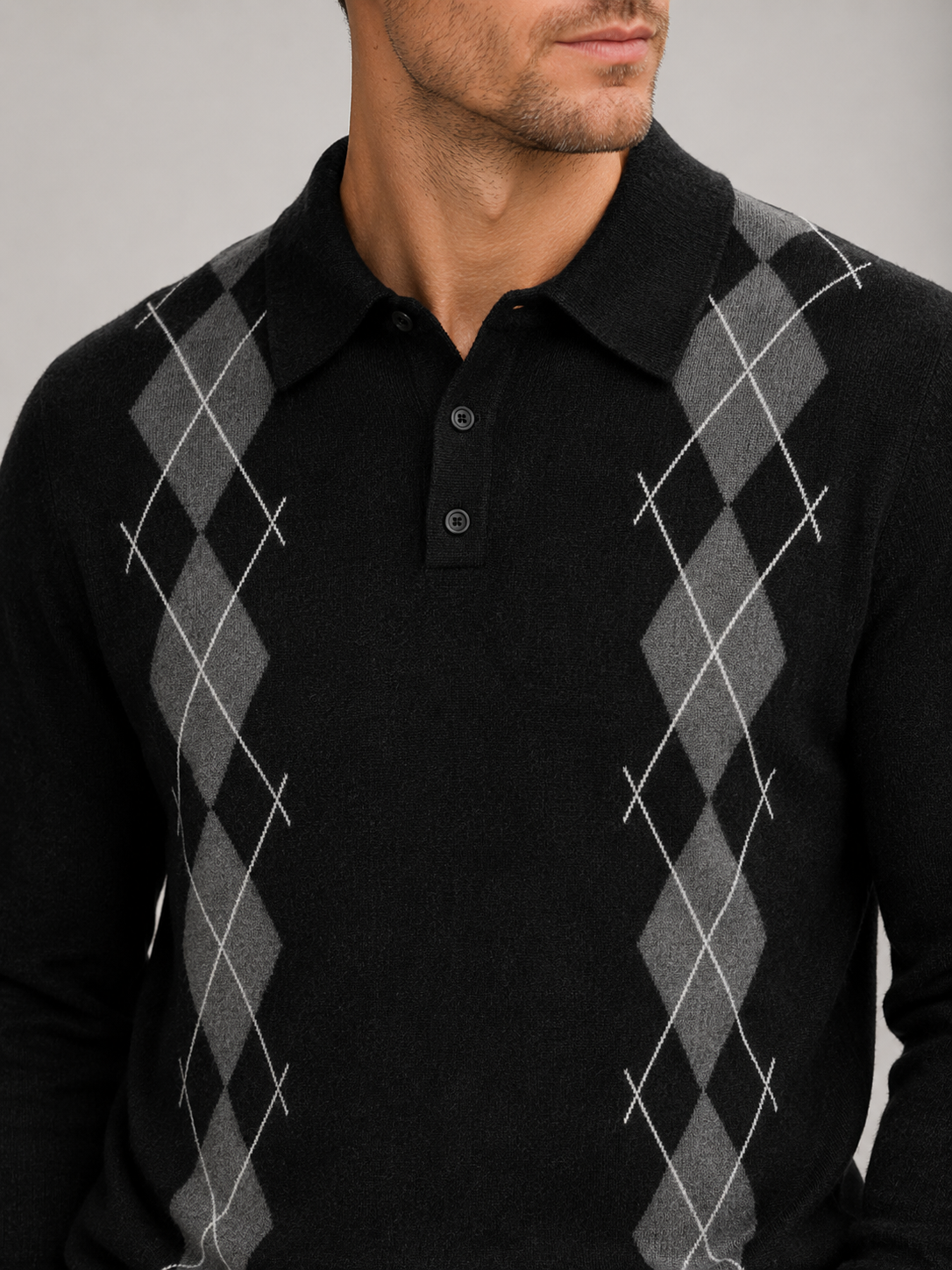 Close-up of a black argyle sweater showing the plaid knit pattern, contrast collar, ribbed cuffs, hem, and premium knit texture