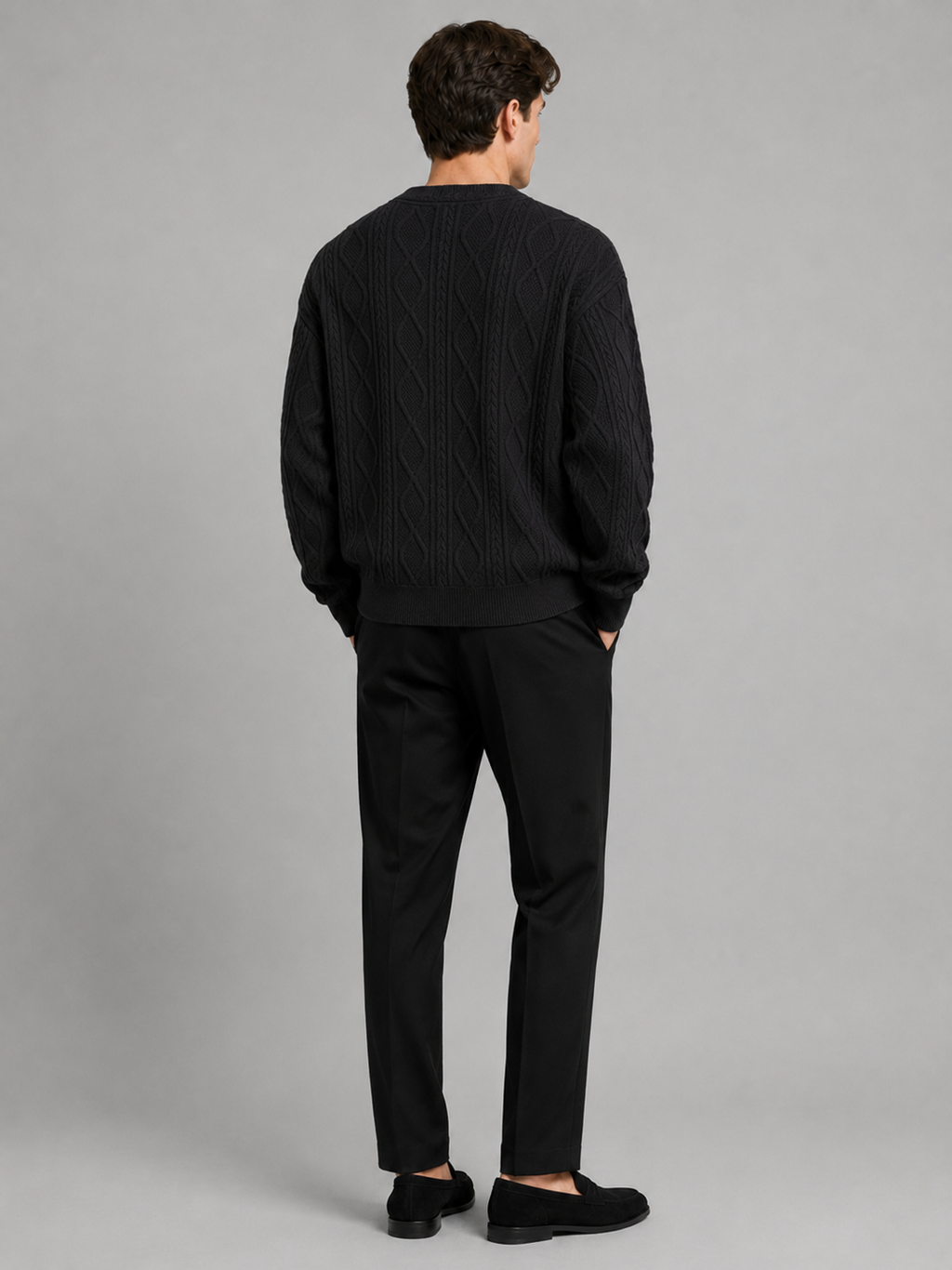 Back view of a man wearing a black cable knit cardigan sweater showing the relaxed oversized fit, long sleeves, and warm knit construction