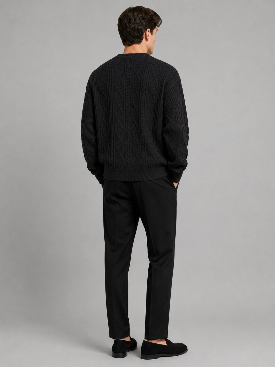 Back view of a man wearing a black cable knit cardigan sweater showing the relaxed oversized fit, long sleeves, and warm knit construction