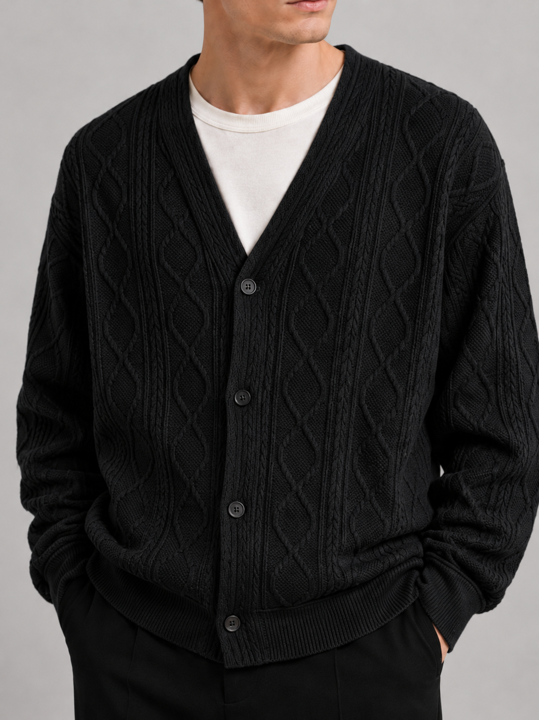 Close-up of a black cable knit cardigan showing the diamond pattern, textured cable knit, V-neckline, front buttons, ribbed cuffs, and hem