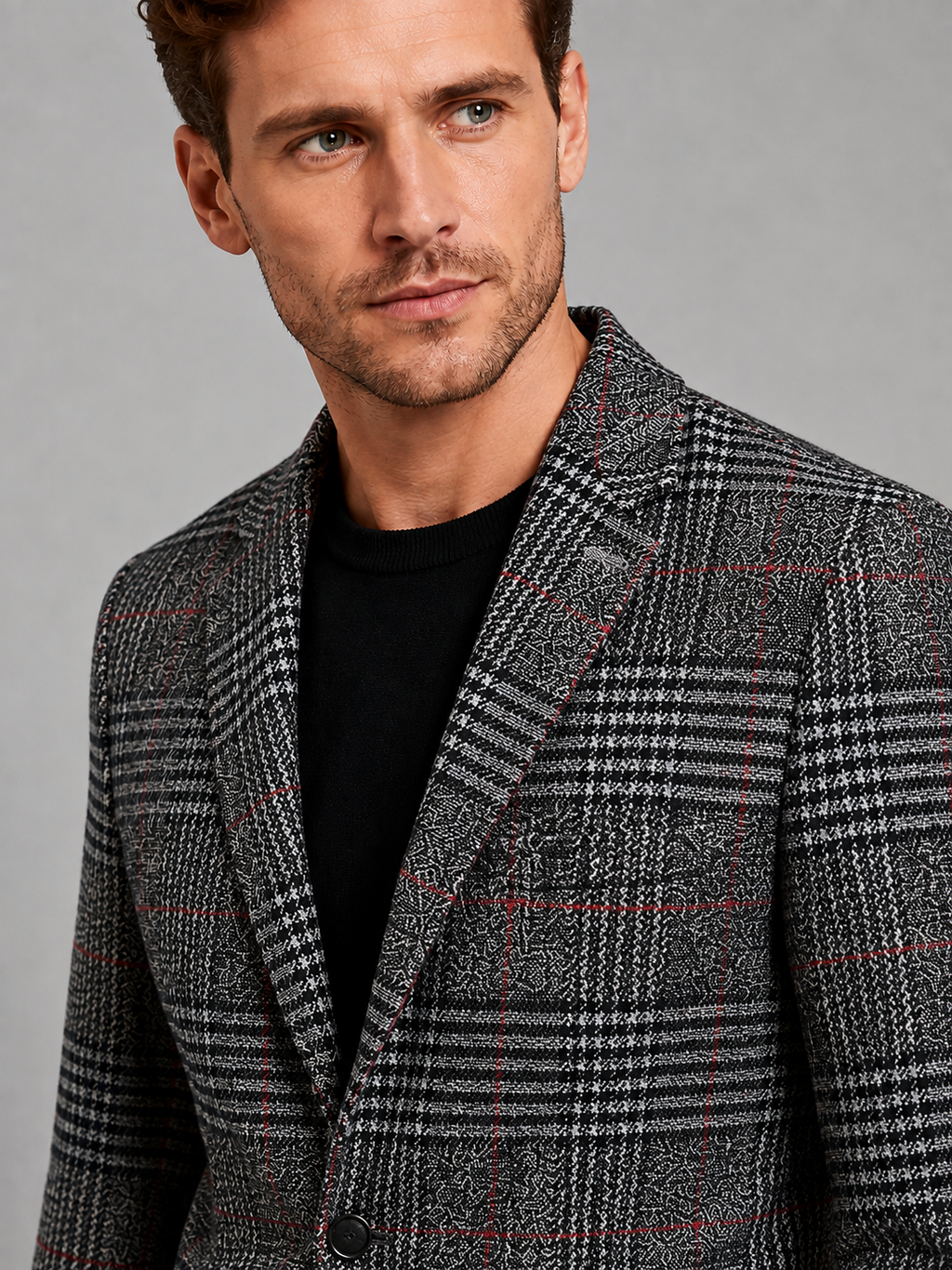Close-up of a black checkered blazer showing the woven check pattern, notched lapel, button closure, premium fabric texture, and tailored stitching