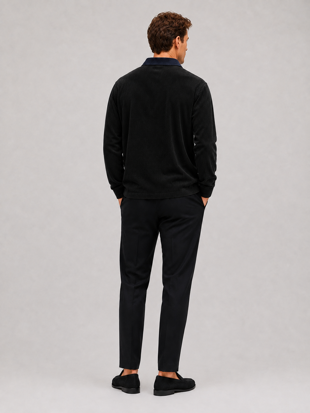 Back view of a man wearing a black corduroy polo shirt showing the long sleeves, relaxed fit, and soft textured fabric