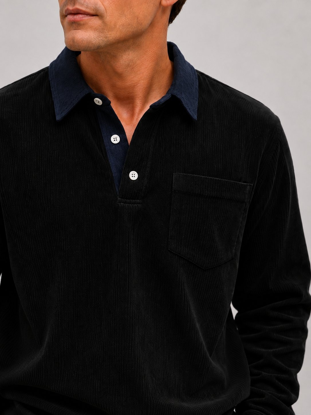 Close-up of a black corduroy polo shirt showing the textured polyester fabric, contrast turn-down collar, button placket, cuffs, and stitching