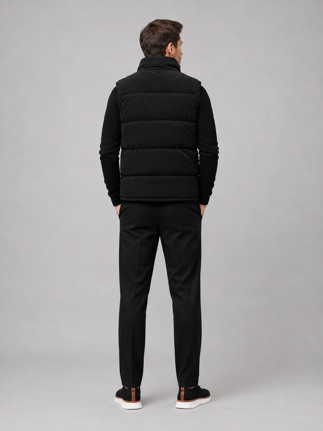 Back view of a man wearing a black corduroy puffer vest showing the sleeveless cut, padded construction, and comfortable fit