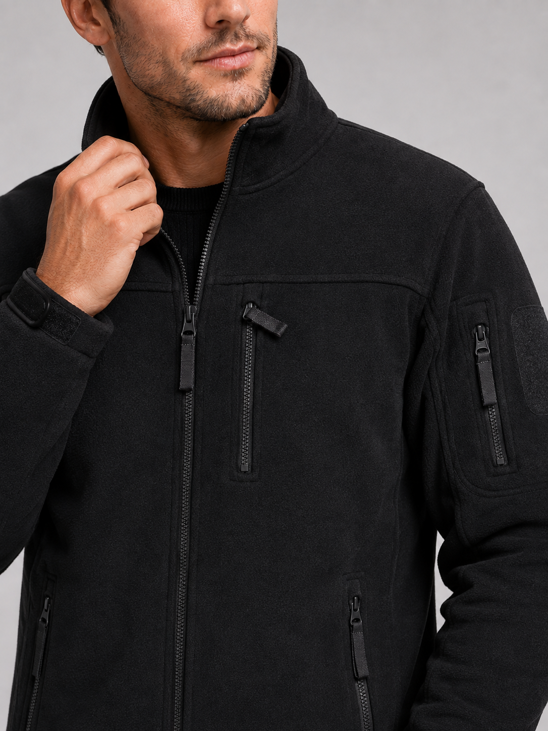 Close-up of a black windproof fleece jacket showing the soft fleece texture, full zipper, zippered pockets, collar, cuffs, hem, and stitching details
