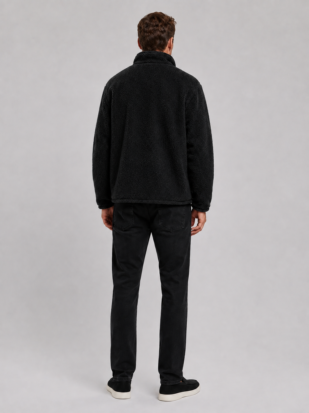 Back view of a man wearing a black fleece jacket showing the relaxed loose fit, long sleeves, stand collar, and soft fleece construction