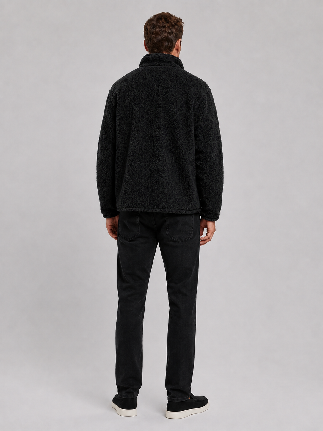 Back view of a man wearing a black fleece jacket showing the relaxed loose fit, long sleeves, stand collar, and soft fleece construction