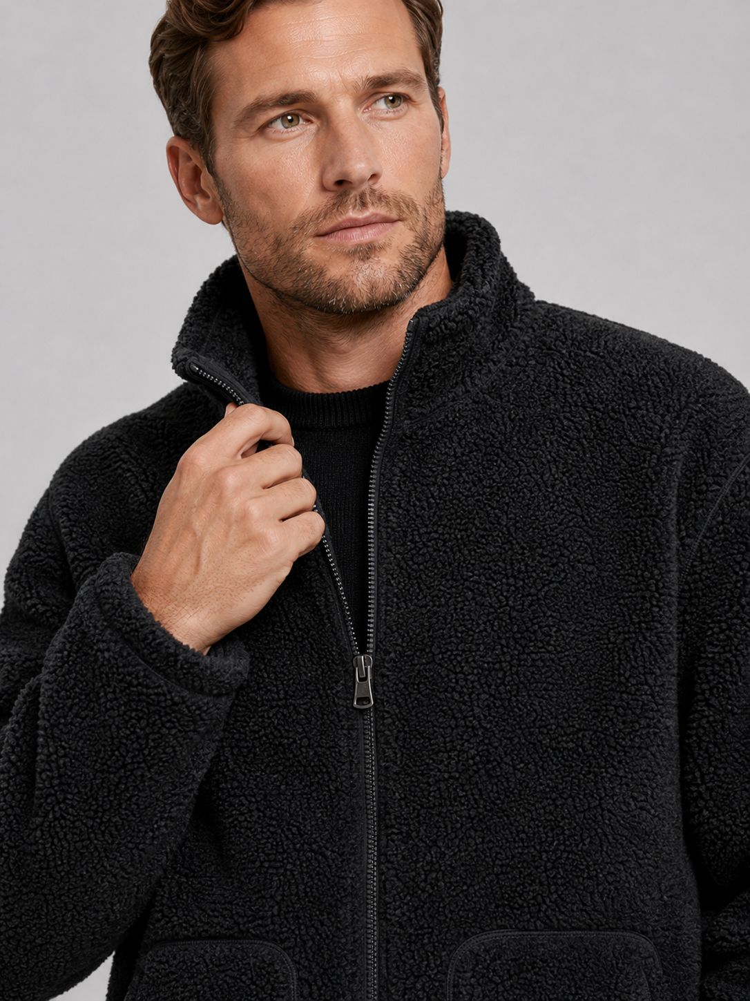 Close-up of a black fleece jacket showing the soft fleece texture, full zipper, stand collar, pockets, cuffs, hem, and stitching details