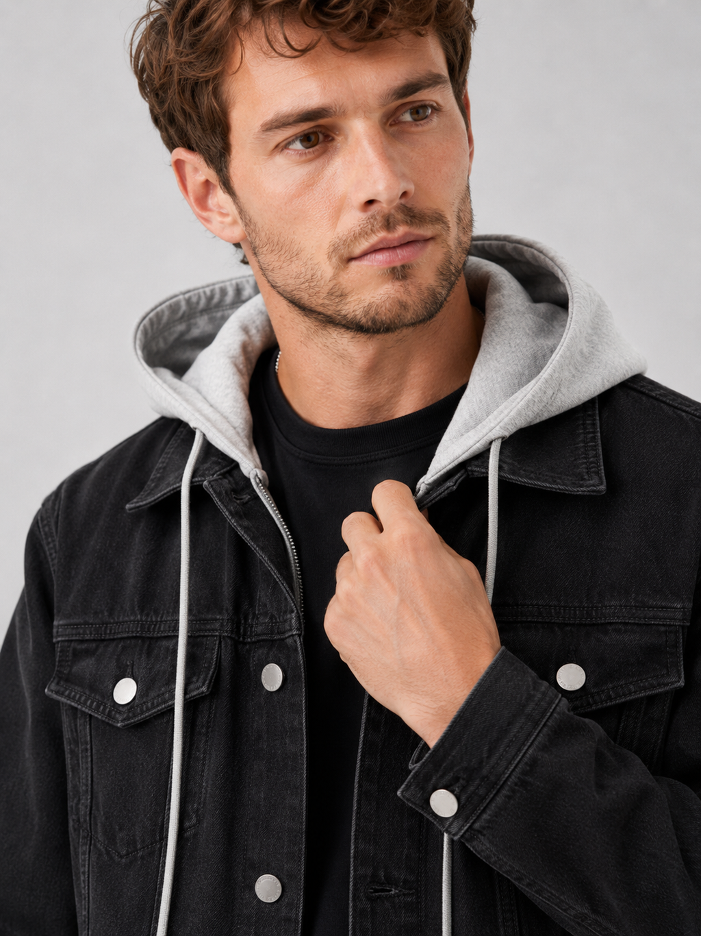 Close up of black denim jacket showing washed fabric texture, detachable hood, and stitching detail