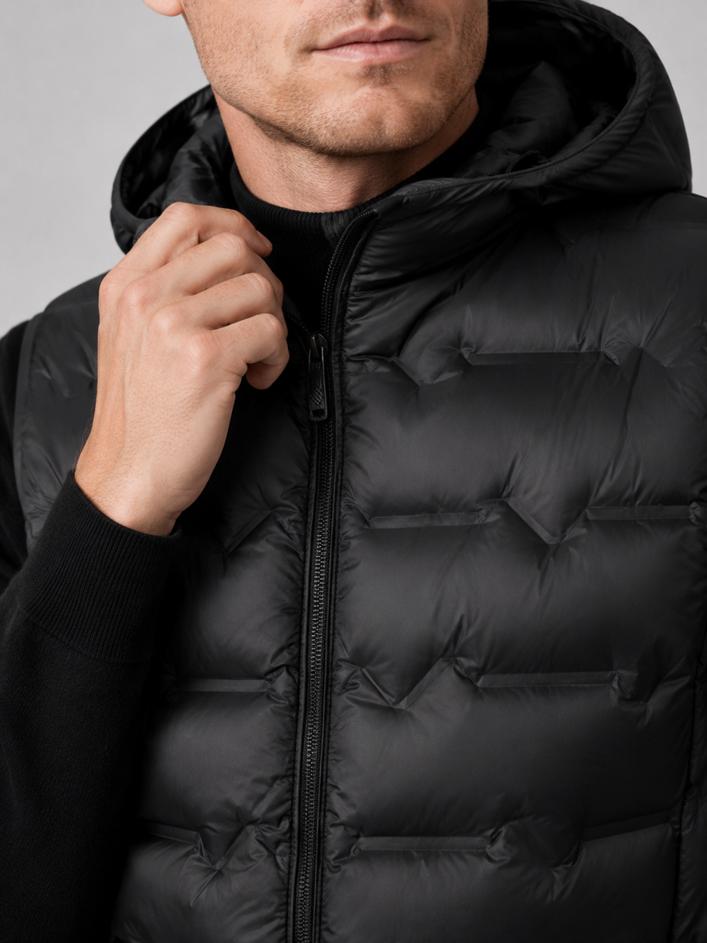Close up of black hooded down vest showing lightweight quilted insulation, attached hood, and weather resistant fabric detail