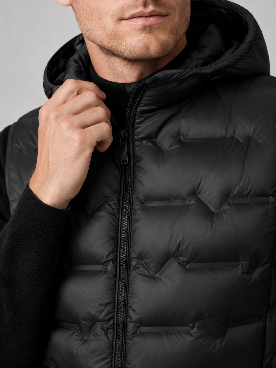 Close up of black hooded down vest showing lightweight quilted insulation, attached hood, and weather resistant fabric detail