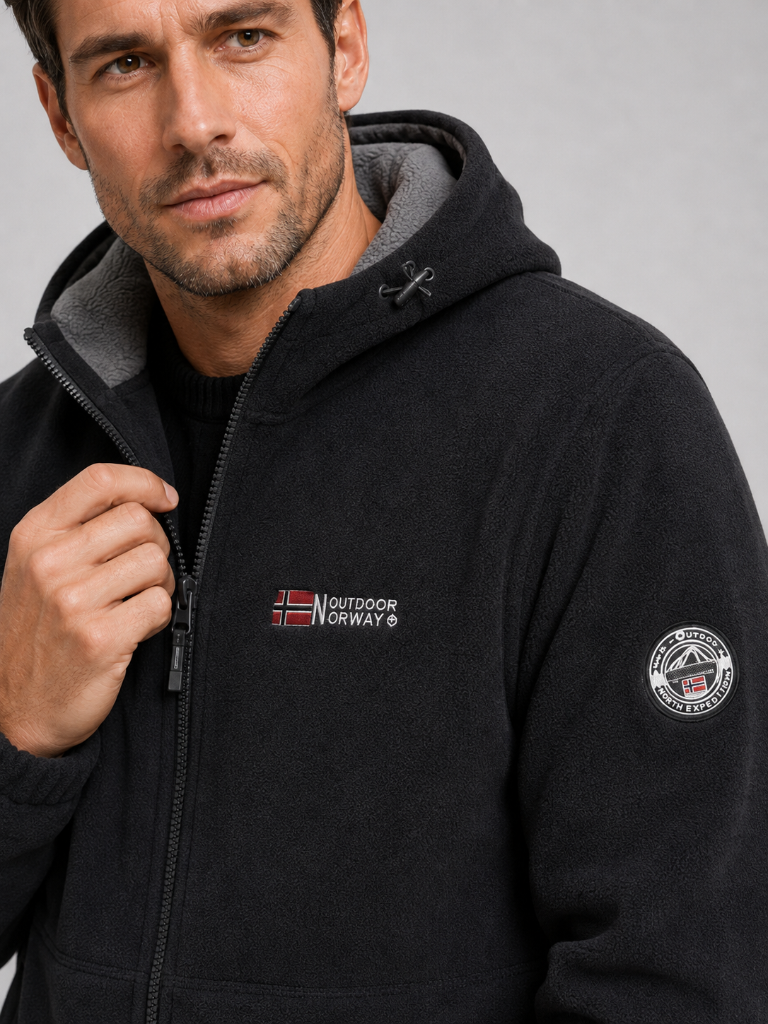 Close-up of a black hooded fleece jacket showing the soft fleece texture, windproof construction, full zipper, hood, pockets, cuffs, and stitching details