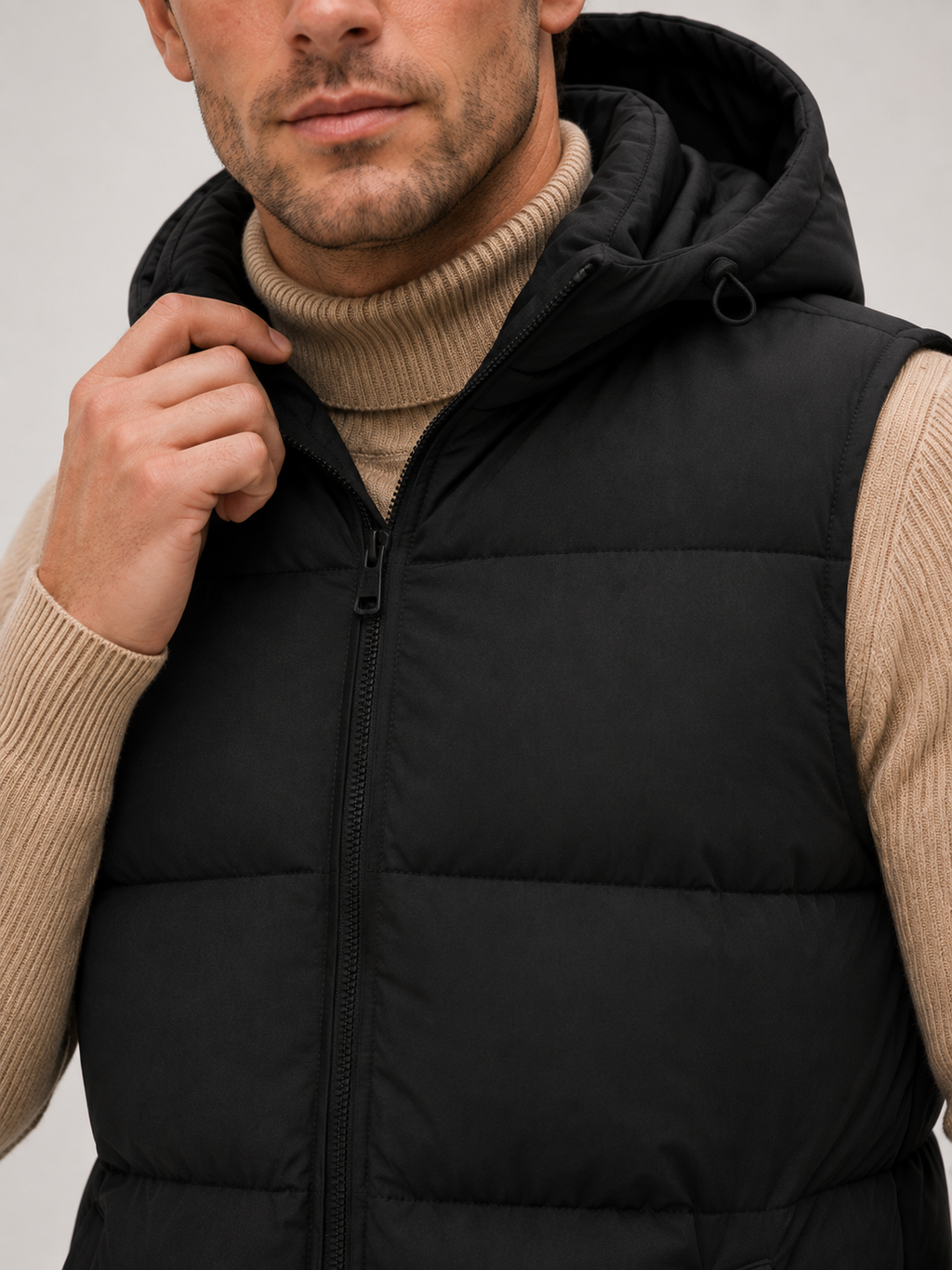 Close-up of a black hooded puffer vest showing the thick quilted insulation, full zipper, hood, pockets, armholes, and stitching