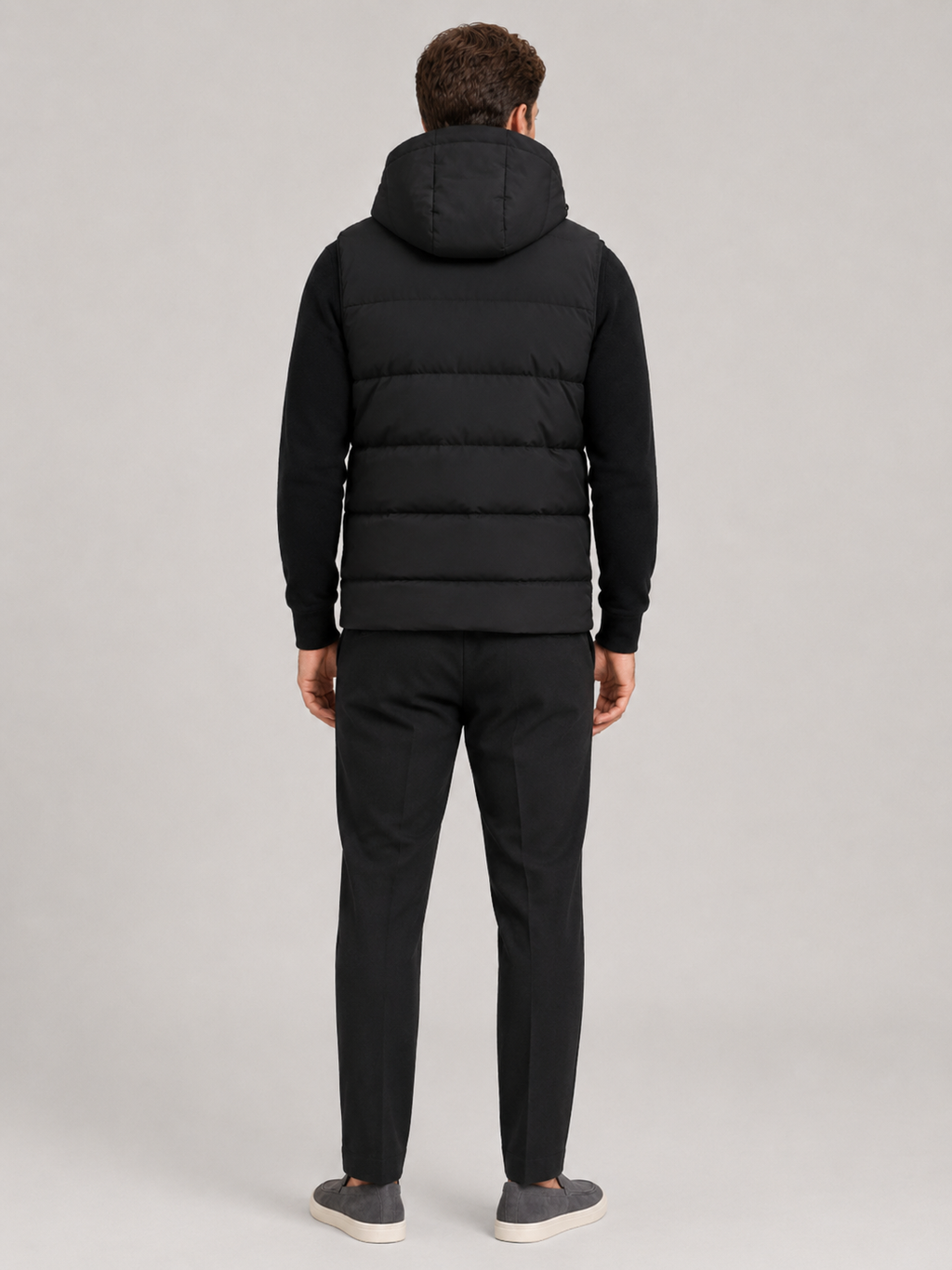 Back view of a man wearing a black hooded puffer vest showing the attached hood, padded construction, sleeveless cut, and comfortable fit