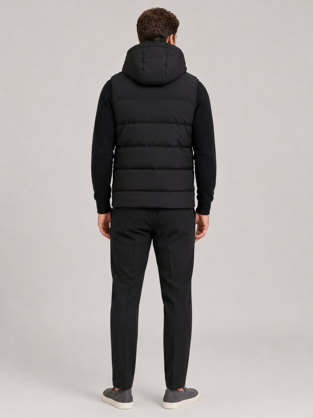 Back view of a man wearing a black hooded puffer vest showing the attached hood, padded construction, sleeveless cut, and comfortable fit