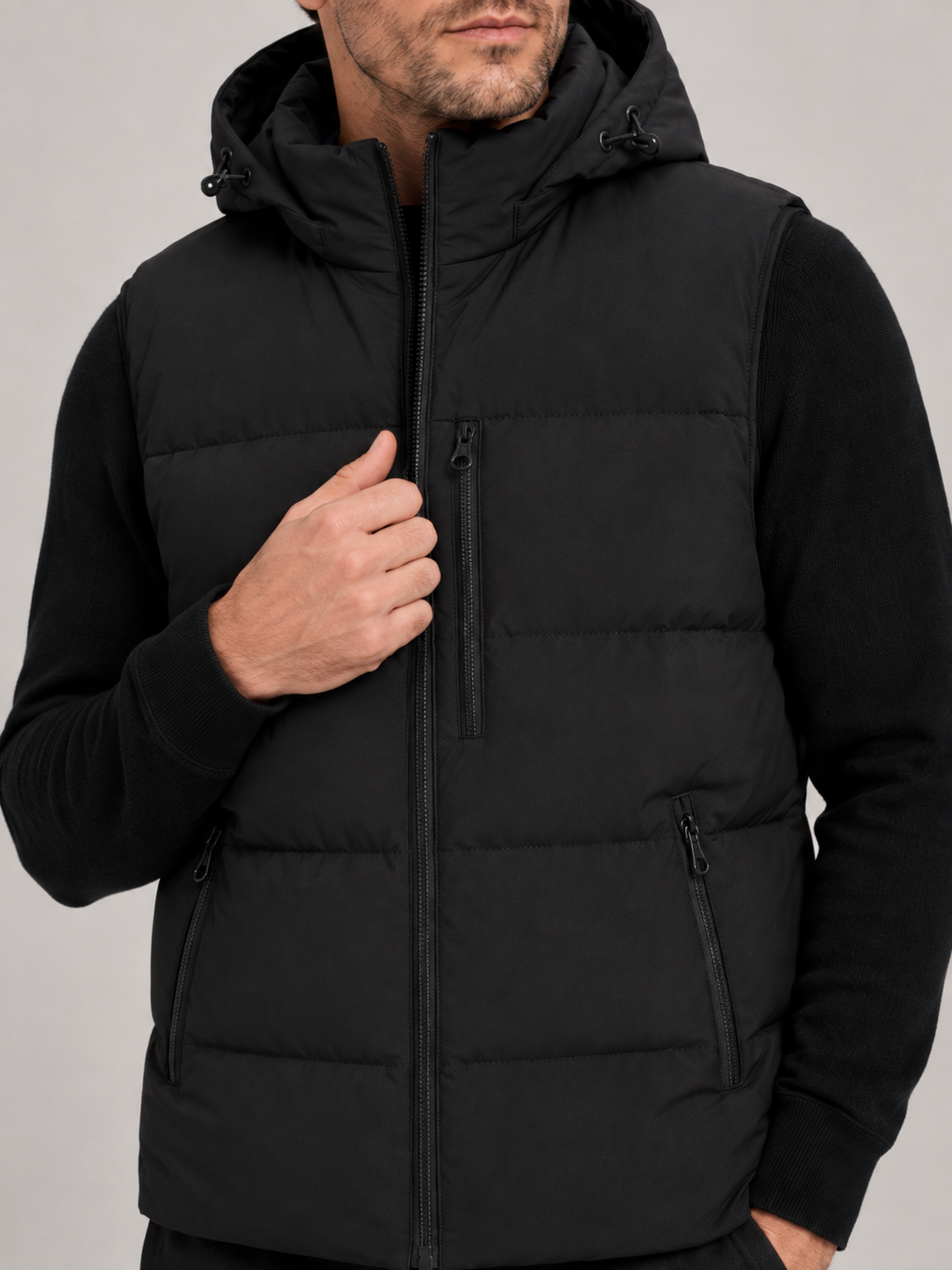 Close-up of a black hooded puffer vest showing the windproof fabric, thick insulation, zipper closure, hood, pockets, armholes, and stitching details