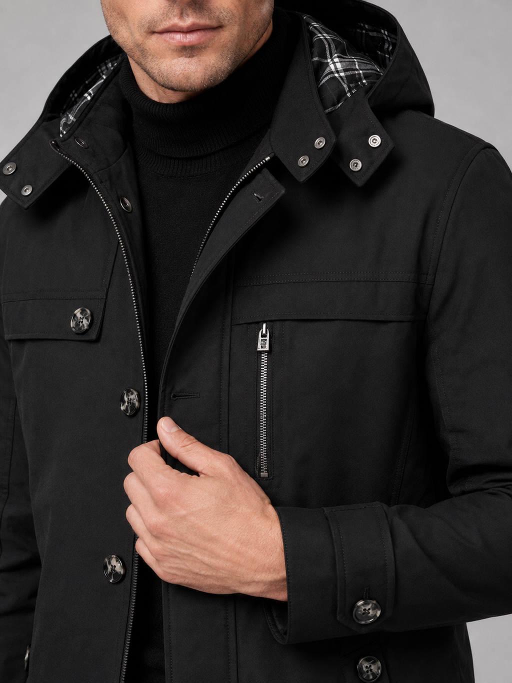 Close up of black hooded trench coat showing thick cotton fabric, attached hood, and button front detail