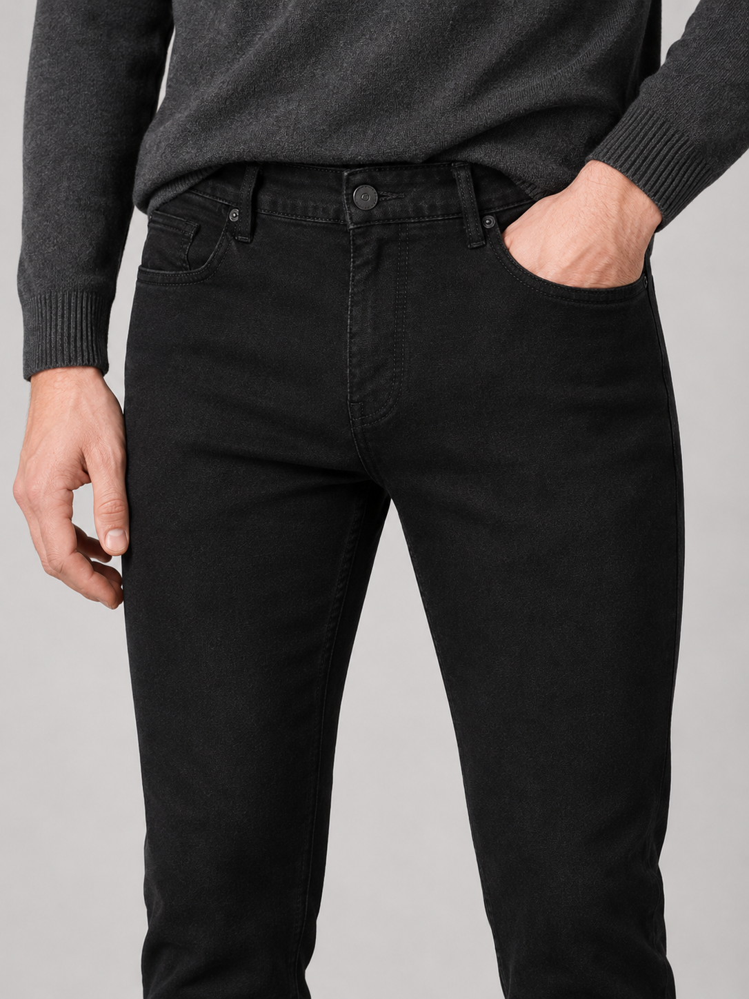 Close-up of black stretch denim jeans showing the denim texture, contrast stitching, zipper fly, button closure, belt loops, and five-pocket construction