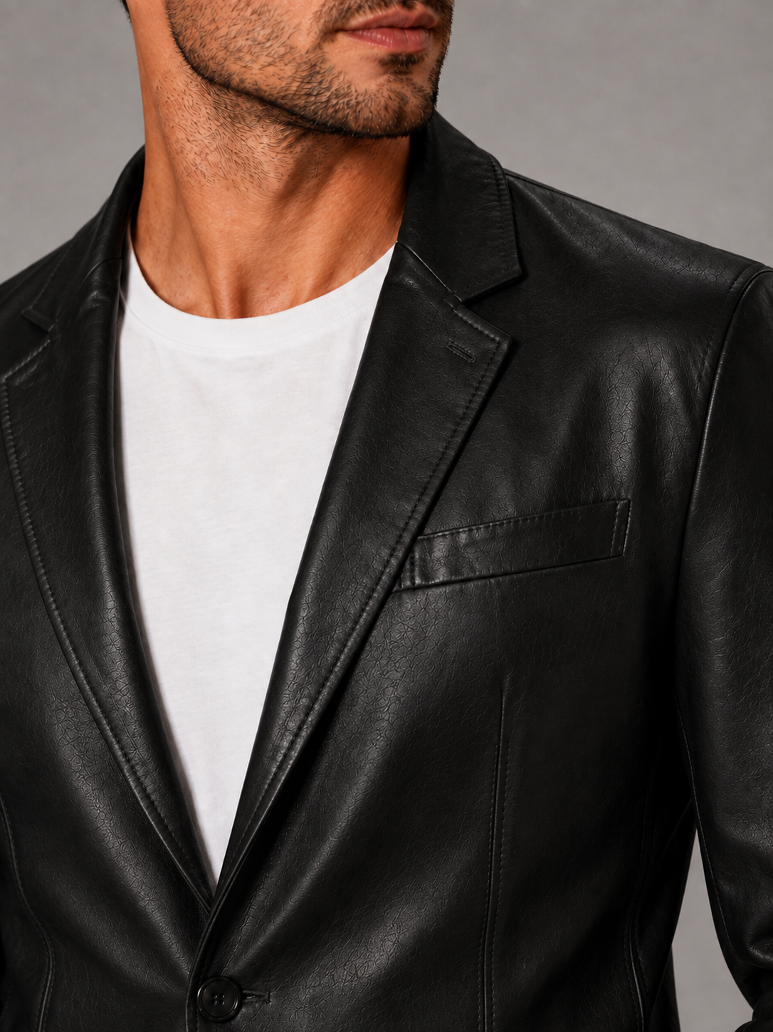 Close-up of a black leather blazer jacket showing the premium leather texture, notched lapel, button closure, tailored stitching, cuffs, and pocket details