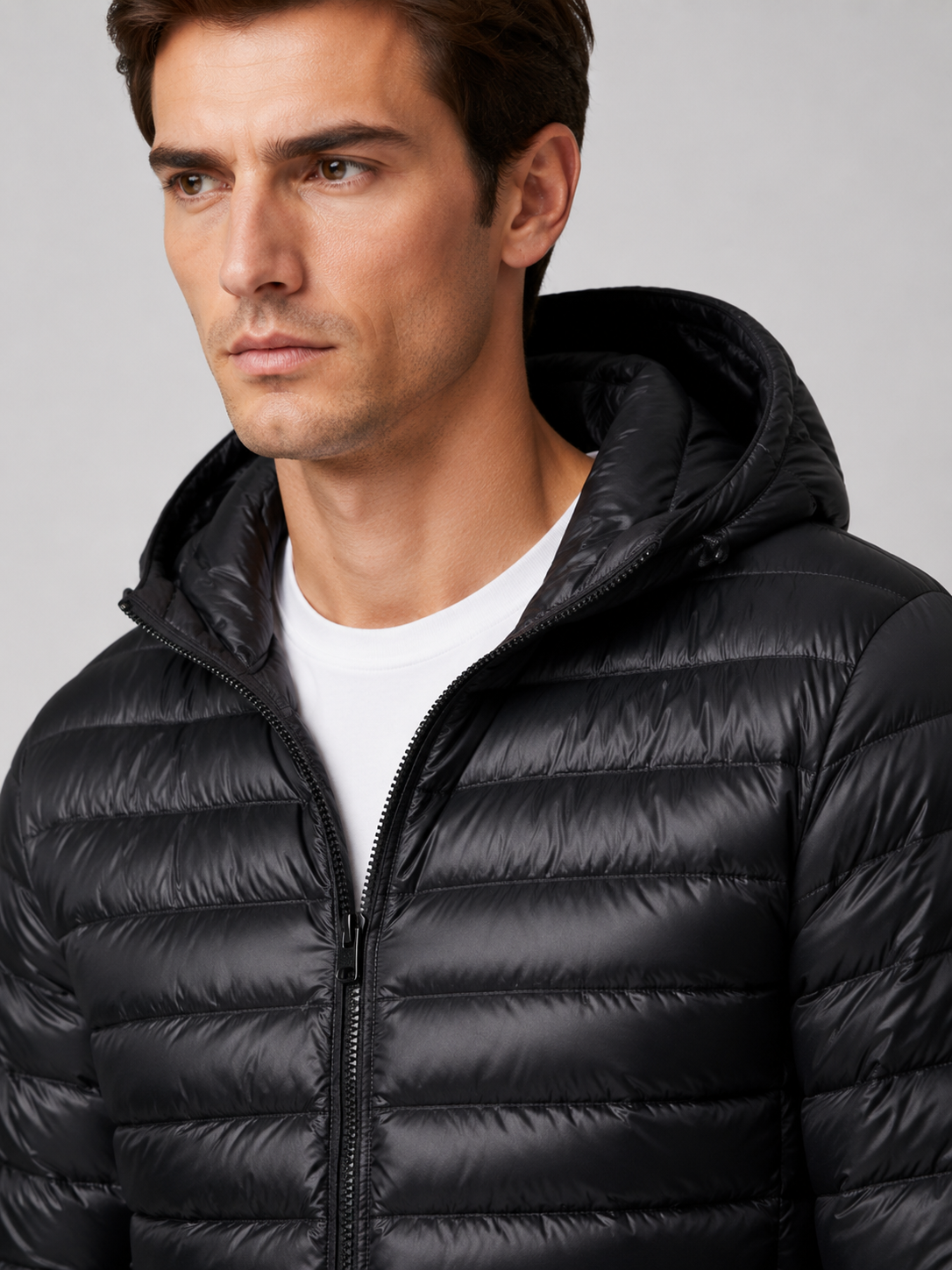 Close up of black hooded down jacket showing lightweight quilted insulation, attached hood, and weather resistant fabric detail