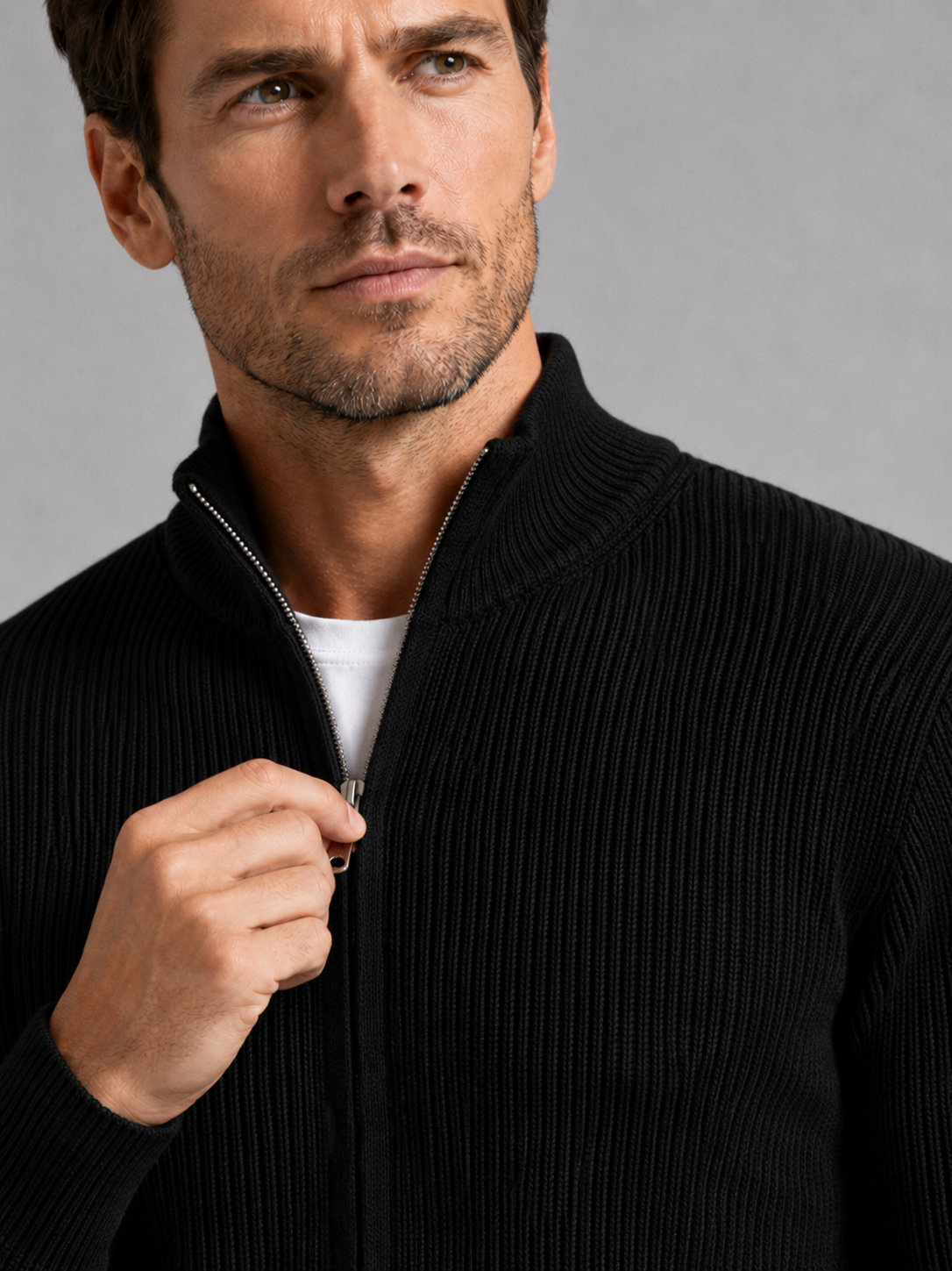 Close-up of a black ribbed knit cardigan showing the textured knit fabric, stand collar, full zipper, ribbed cuffs, hem, and stitching details