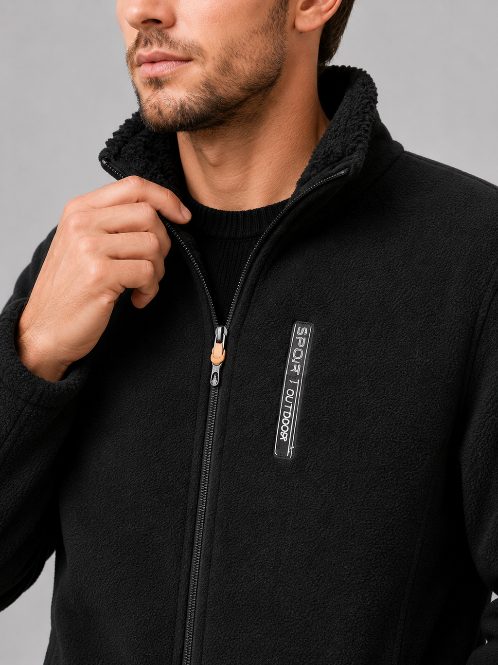 Close-up of a black polar fleece jacket showing the soft fleece texture, windproof construction, full zipper, stand collar, pockets, cuffs, and stitching details