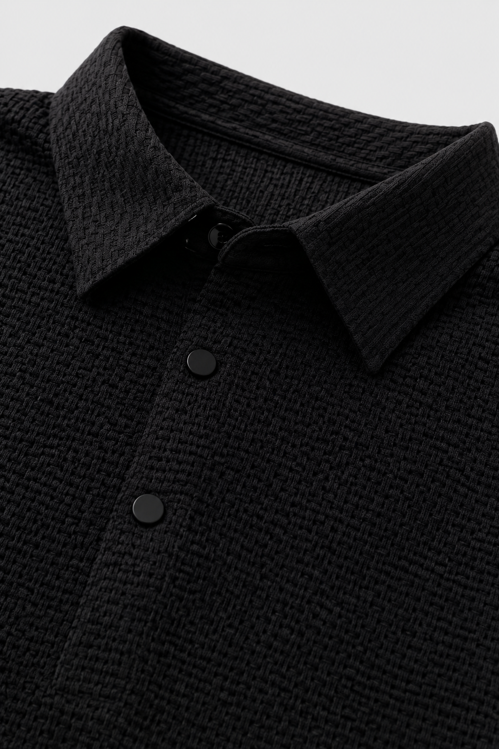 Close up of black textured knit polo fabric showing breathable weave and button placket detail