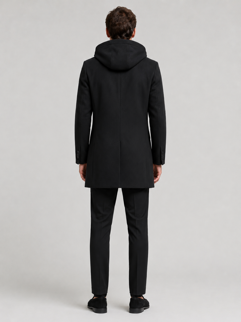 Backside photo of a man wearing a black wool hooded trench coat, showing the hood, back seam, coat length, and tailored winter fit