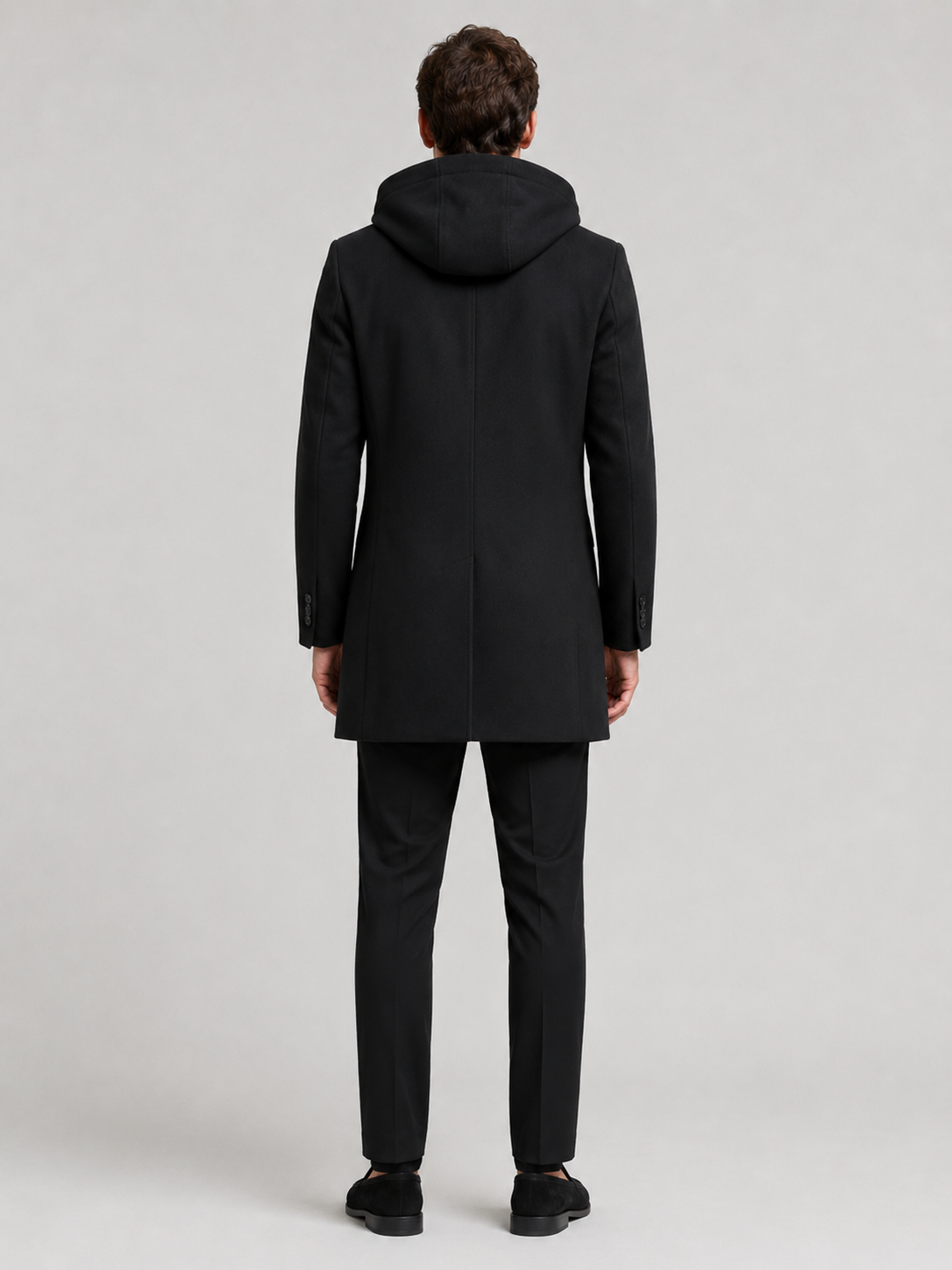 Backside photo of a man wearing a black wool hooded trench coat, showing the hood, back seam, coat length, and tailored winter fit