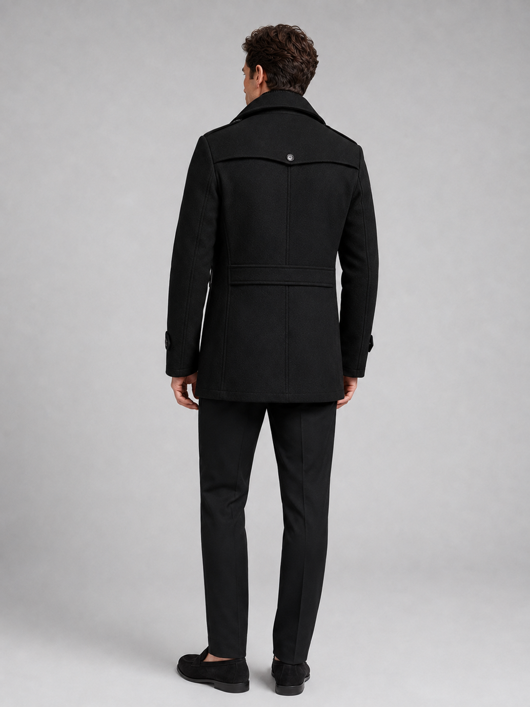 Back view of a man wearing a black wool coat showing the structured shoulders, long silhouette, and tailored fit
