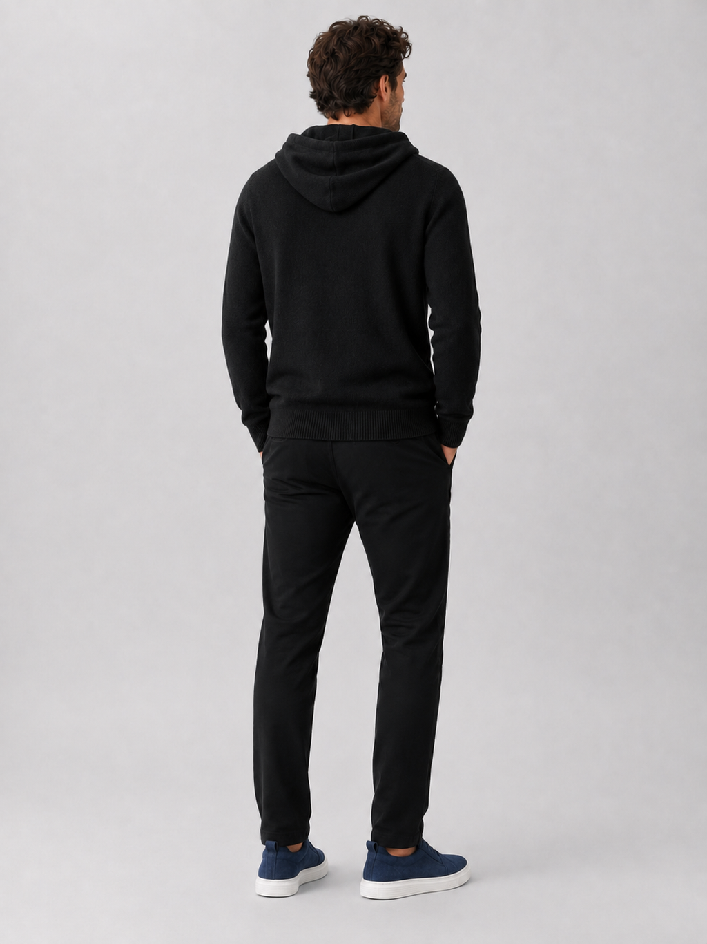 Back view of a man wearing a black wool hoodie sweater showing the attached hood, long sleeves, and relaxed fit