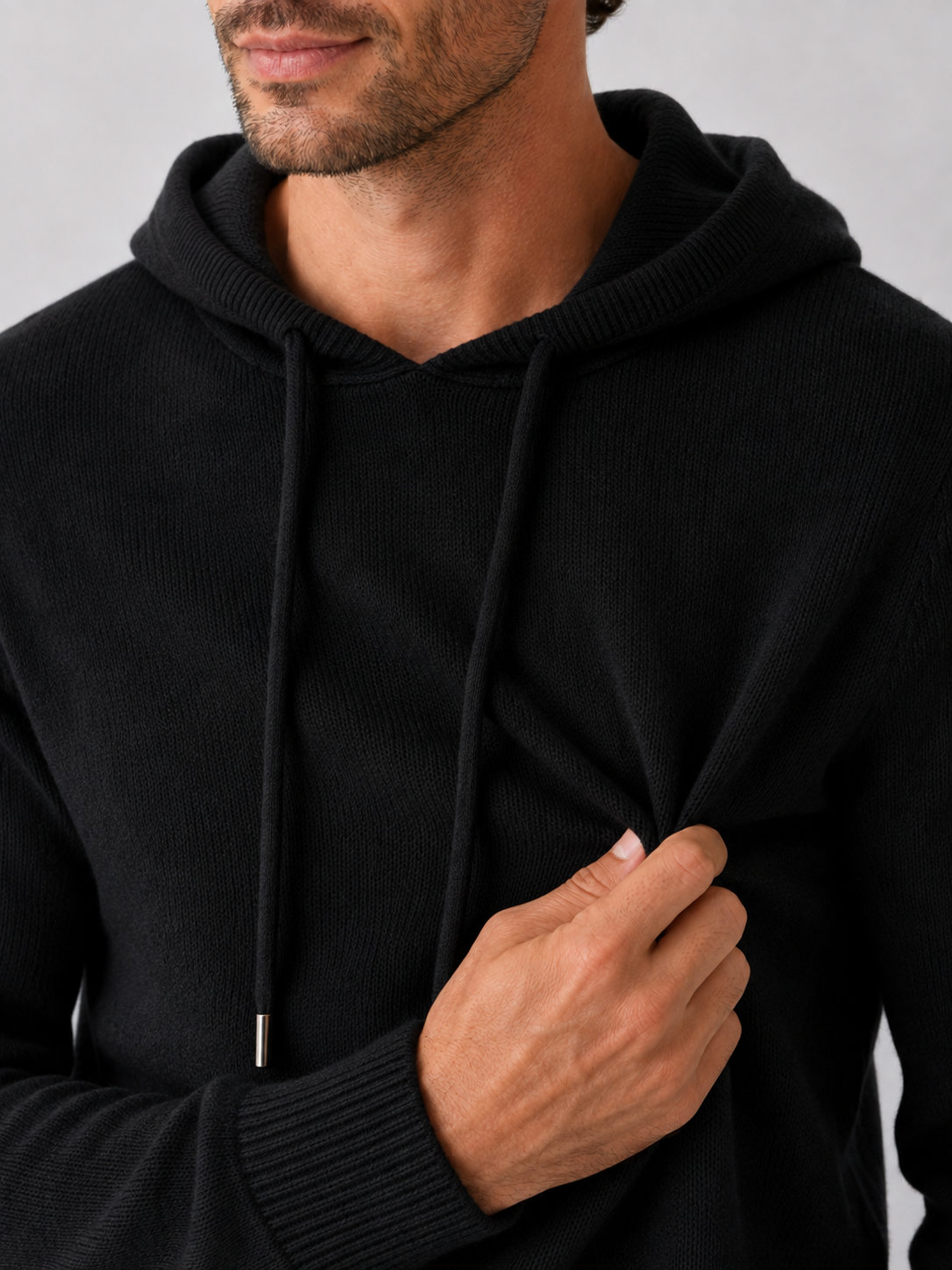 Close-up of a black wool hoodie sweater showing the soft knit texture, hood, ribbed cuffs, hem, and stitching details