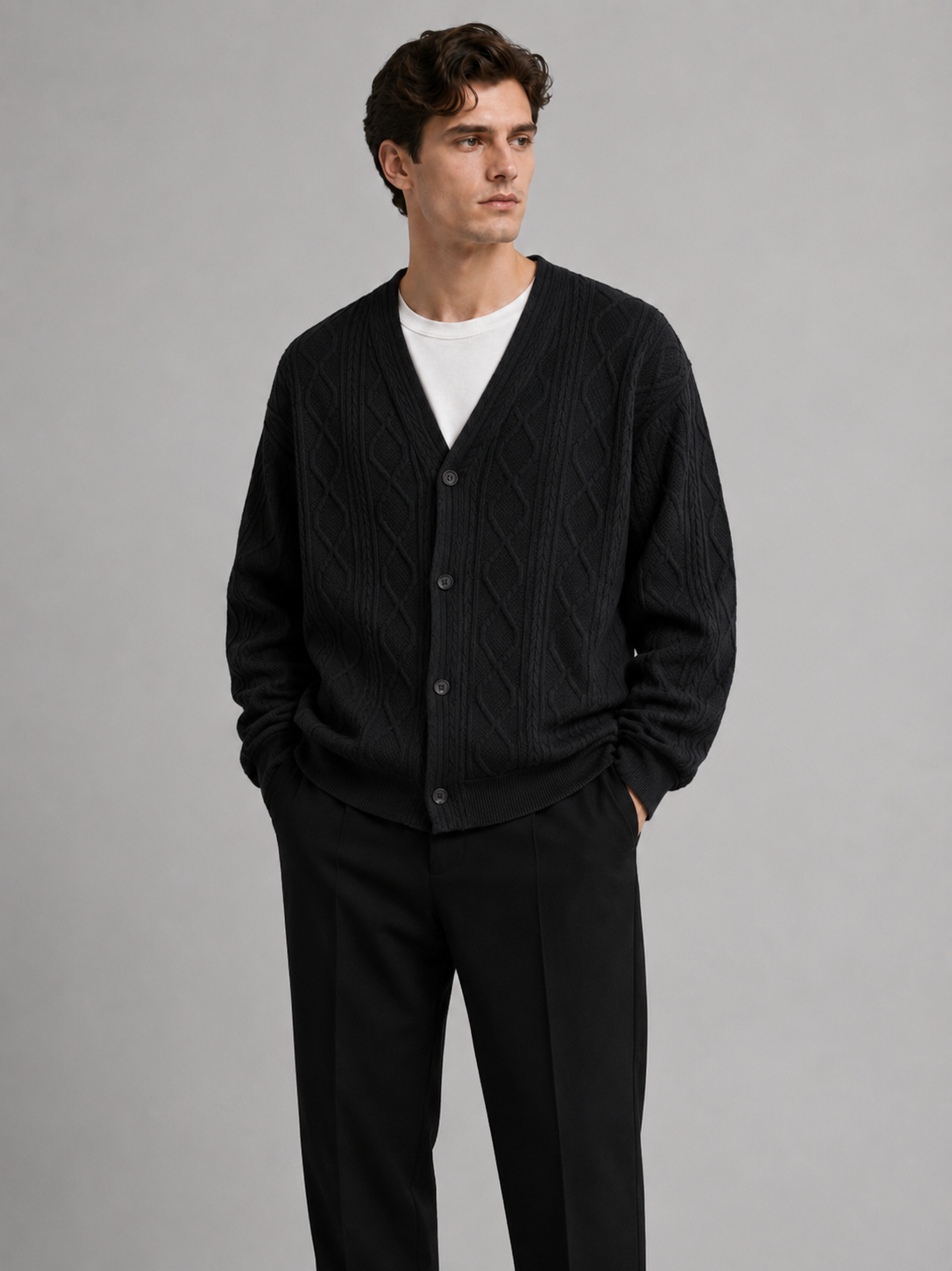 Front view of a man wearing a black cable knit cardigan sweater with a V-neck, diamond pattern, button-front design, and oversized fit