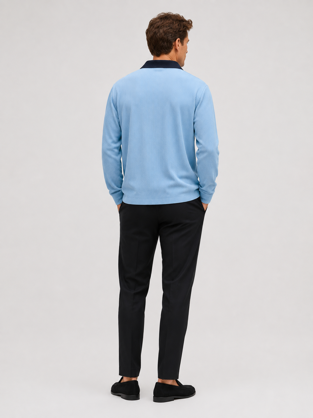 Back view of a man wearing a blue corduroy polo shirt showing the long sleeves, relaxed fit, and soft textured fabric