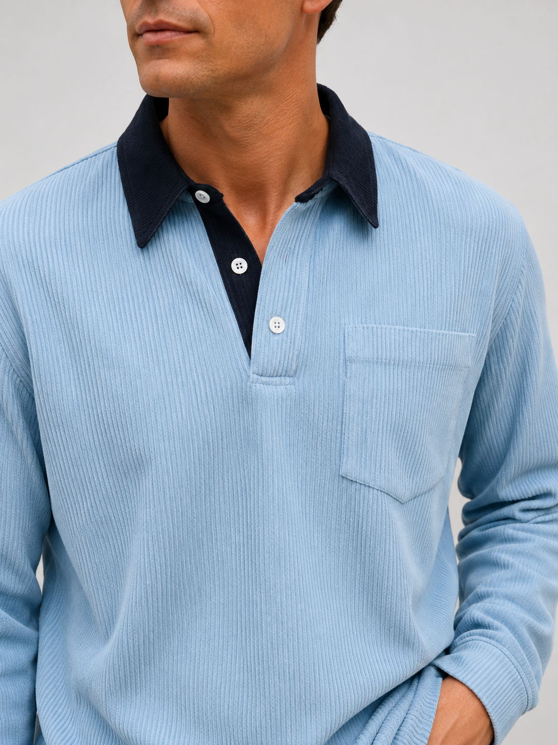 Close-up of a blue corduroy polo shirt showing the textured polyester fabric, contrast turn-down collar, button placket, cuffs, and stitching