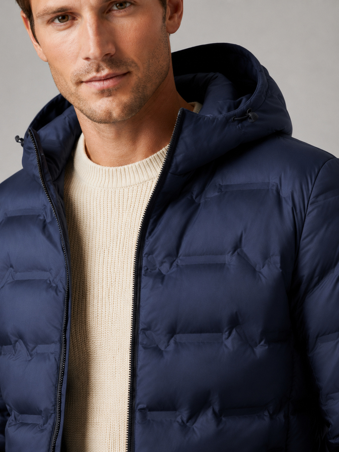 Close up of blue duck down jacket showing lightweight quilted insulation, attached hood, and weather resistant fabric detail