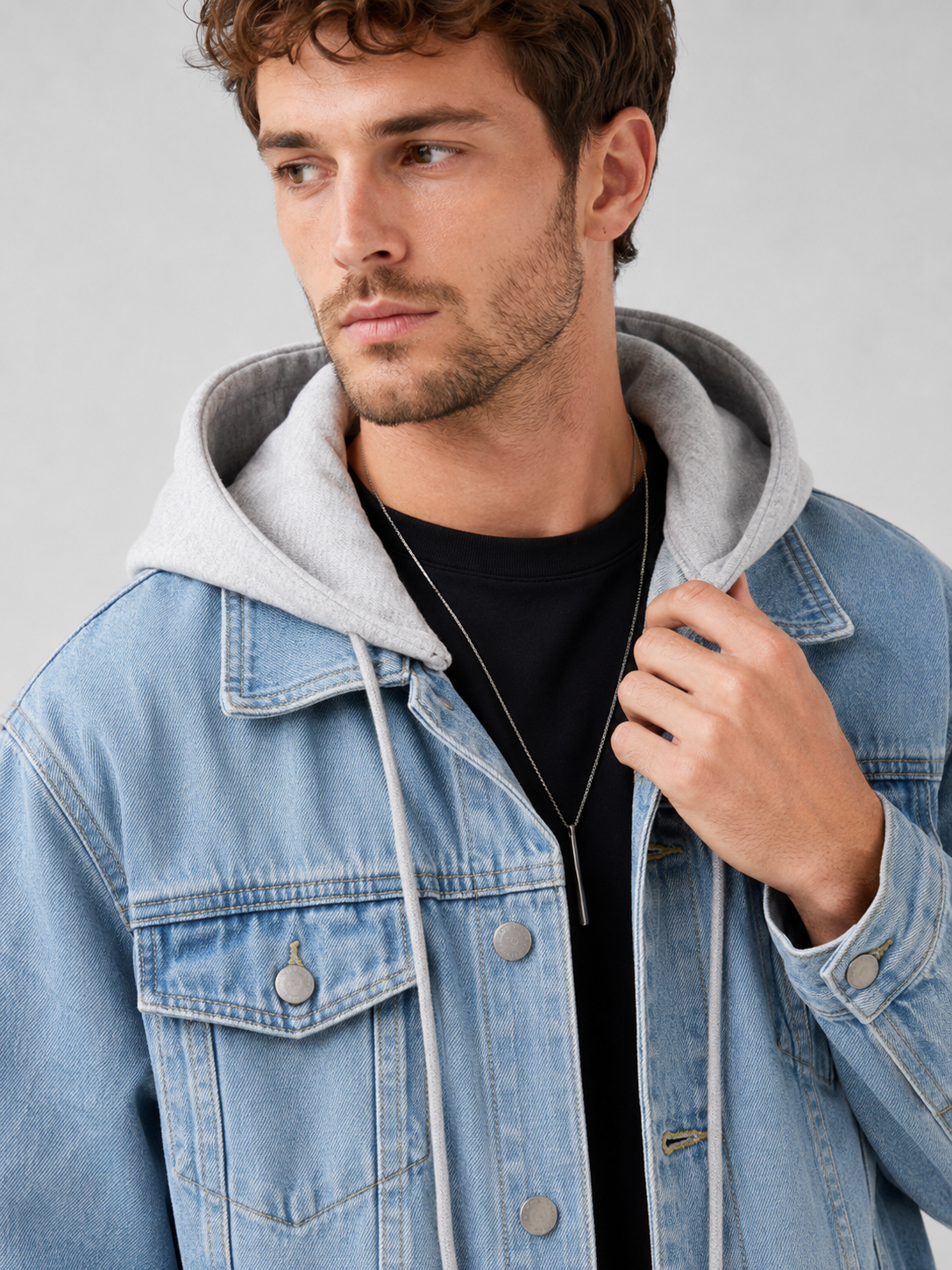 Close up of blue denim jacket showing washed fabric texture, detachable hood, and stitching detail