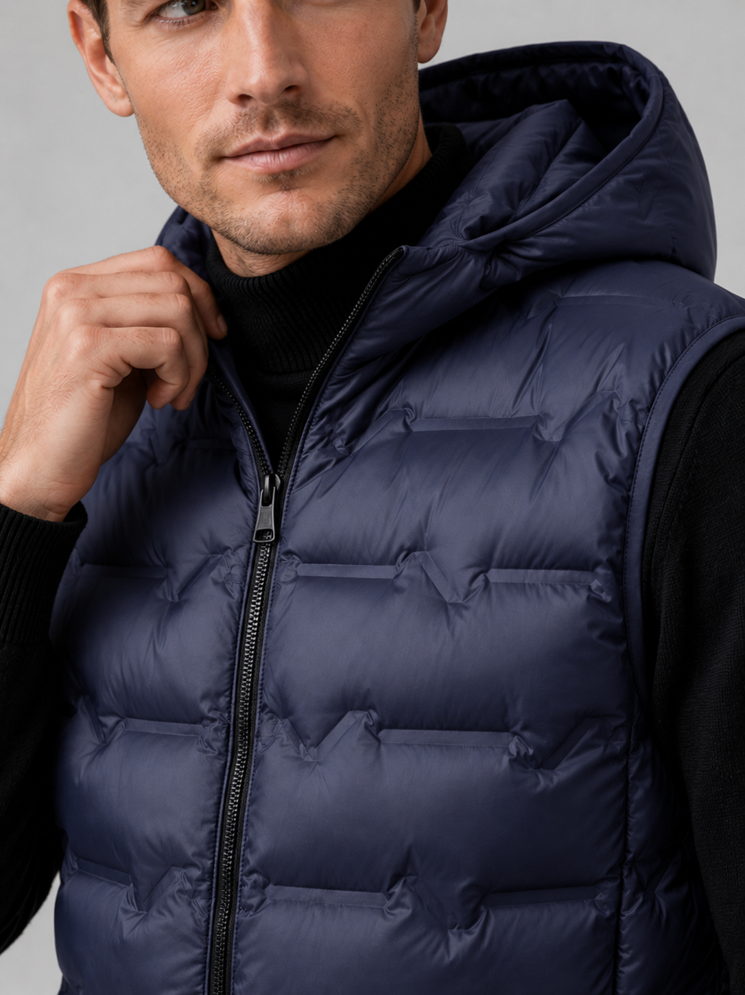 Close up of navy hooded down vest showing lightweight quilted insulation, attached hood, and weather resistant fabric detail