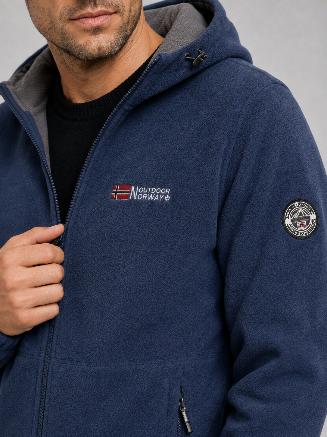 Close-up of a blue hooded fleece jacket showing the soft fleece texture, windproof construction, full zipper, hood, pockets, cuffs, and stitching details