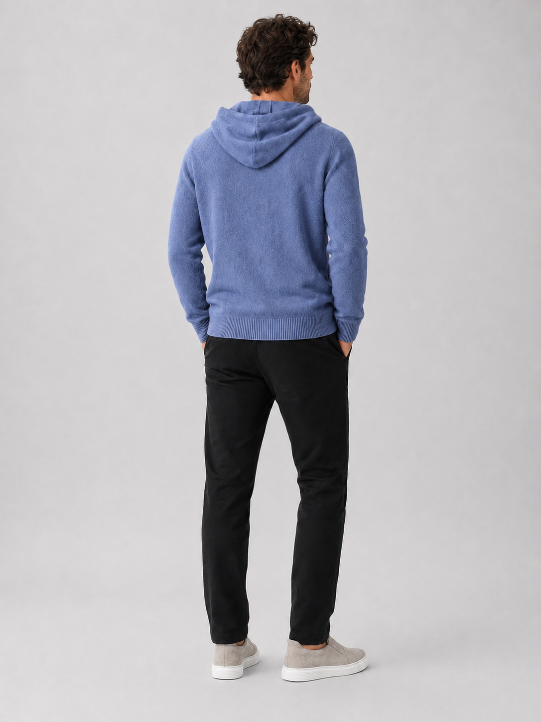 Back view of a man wearing a blue wool hoodie sweater showing the attached hood, long sleeves, and relaxed fit