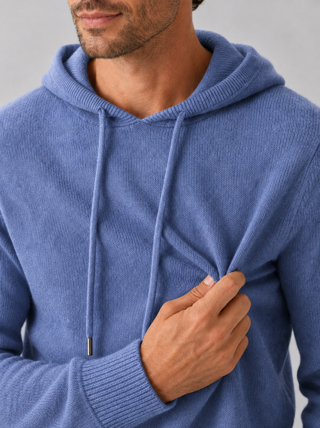 Close-up of a blue wool hoodie sweater showing the soft knit texture, hood, ribbed cuffs, hem, and stitching details